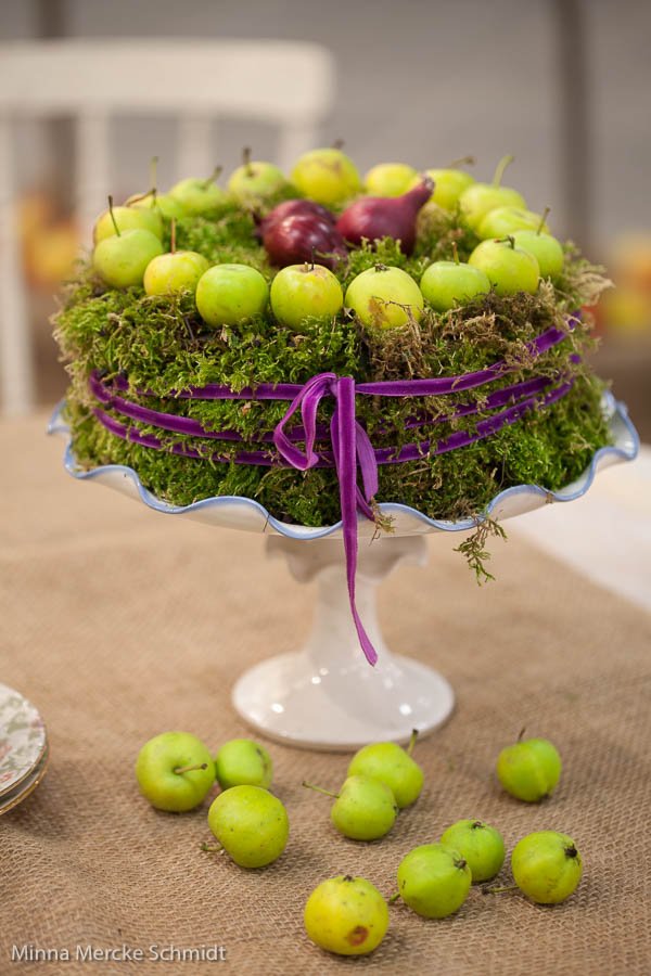 Sammalkakku jossa koristeena pieniä vihreitä omenoita ja punasipulia.